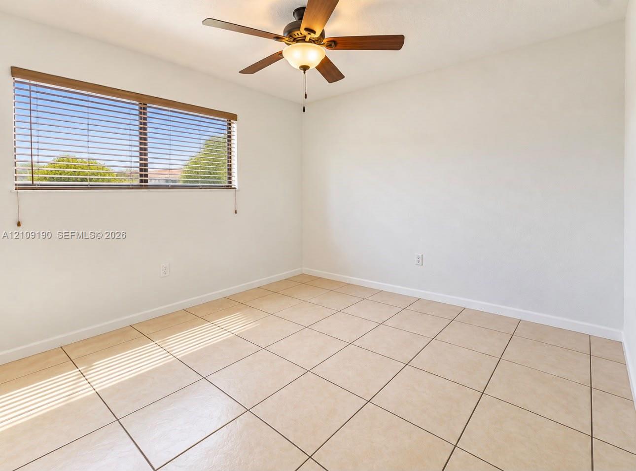 Neutral-toned tile flooring, oversized horizontal window with blinds, and ceiling fan with integrated light fixture