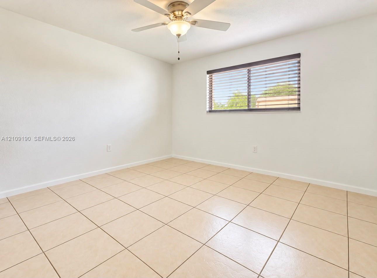 Neutral-toned tile flooring, ceiling fan with integrated lighting, and a horizontal window featuring slatted blinds