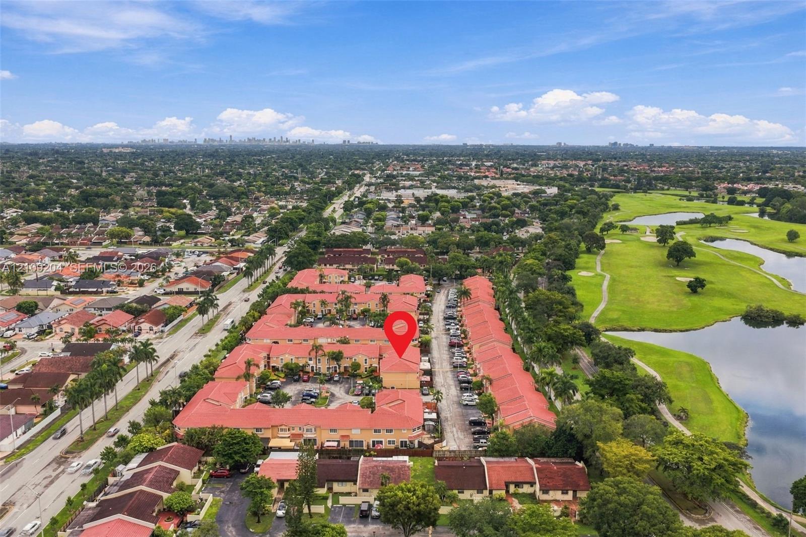 Aerial view of a residential community featuring red tile roofing, paved parking areas, and proximity to expansive golf course grounds with water features