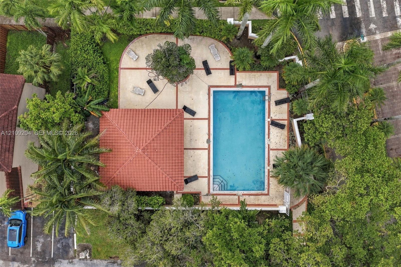Rectangular swimming pool with integrated steps, tiled-roof covered patio, and expansive concrete pool deck surrounded by mature landscaping