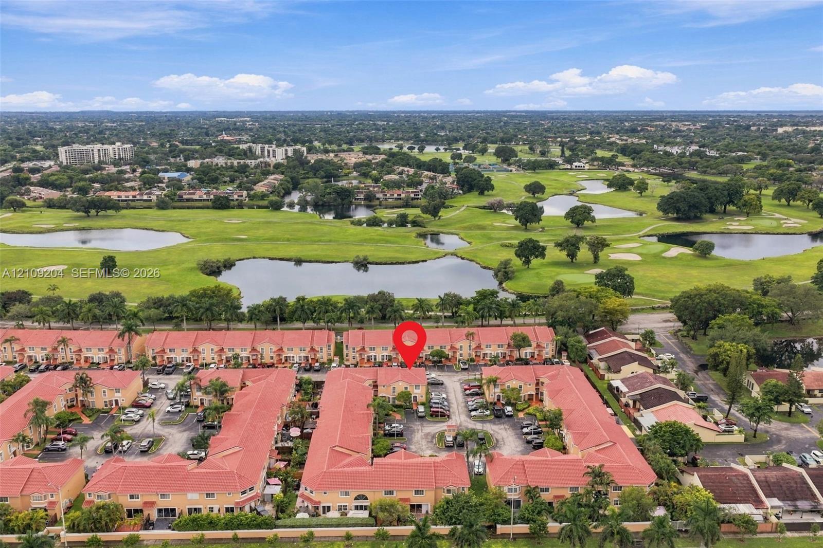 Aerial perspective of a multi-unit residential community featuring red-tile rooflines, stucco facades, and paved parking areas, situated in proximity to golf course greens and ponds