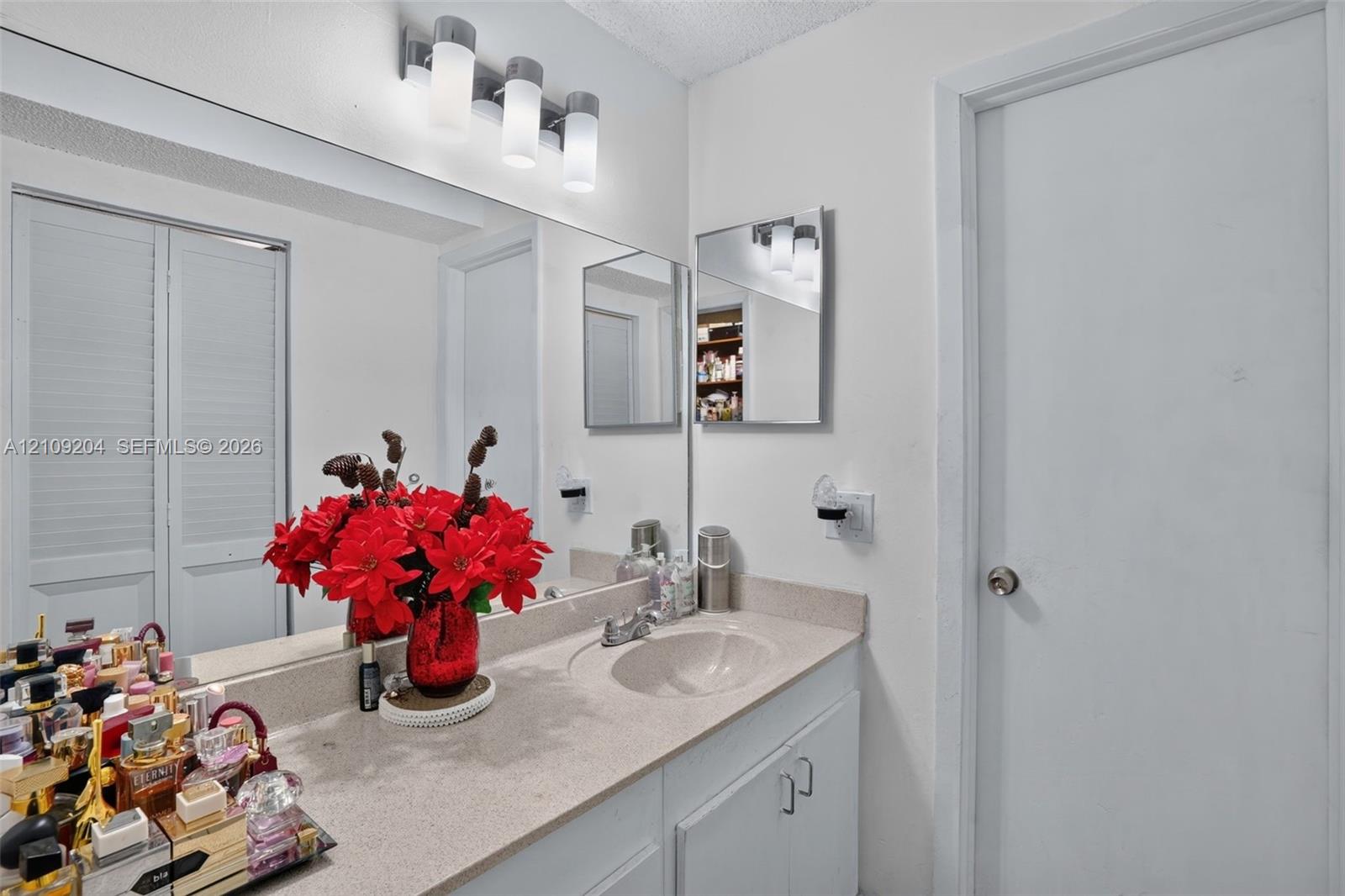 Vanity featuring a stone-composite countertop with an integrated basin, white cabinetry, a large wall-mounted mirror, and a four-light fixture