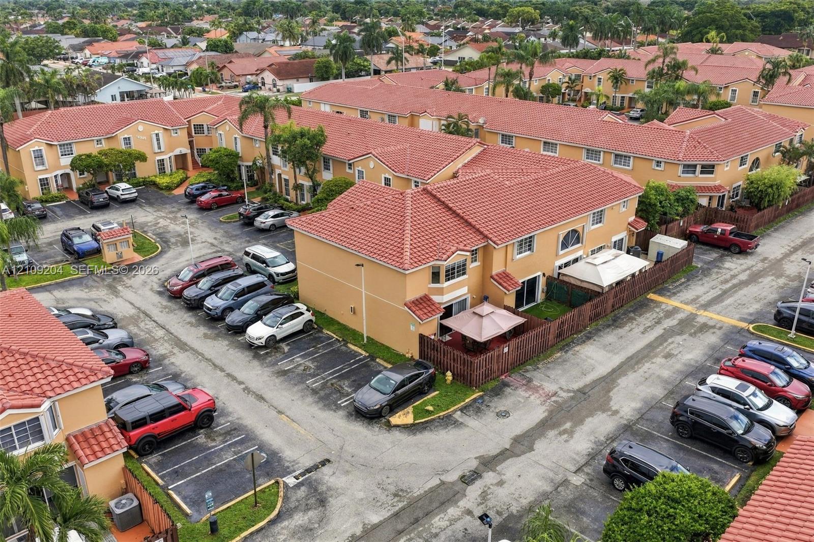 Two-story multi-family exterior featuring a terracotta-colored tiled roof, stucco facade, private fenced-in patio, and designated surface parking Two-story multi-family exterior featuring a terracotta-colored tiled roof, stucco facade, private fenced-in patio, and designated surface parking