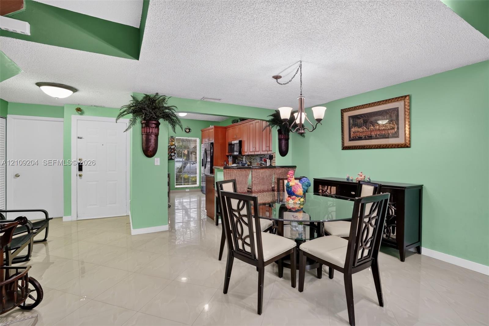 Open-concept interior featuring large-format ceramic tile flooring, recessed ceiling lighting, a multi-arm chandelier, and wood-finish cabinetry