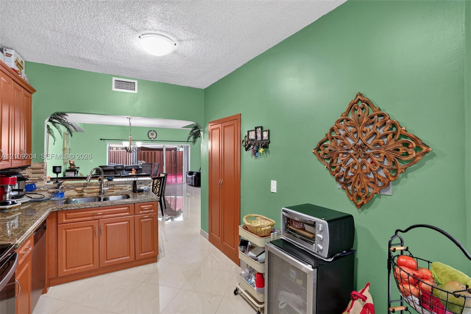 Kitchen featuring wood cabinetry, stone countertops, a dual-basin stainless steel sink, polished tile flooring, and a built-in pantry