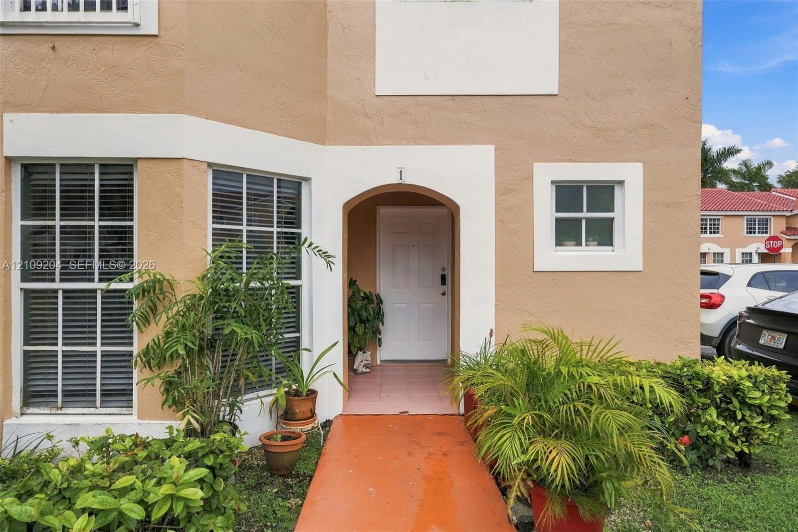 Stucco exterior facade featuring a covered entryway, arched doorway, multi-pane windows, and white architectural trim