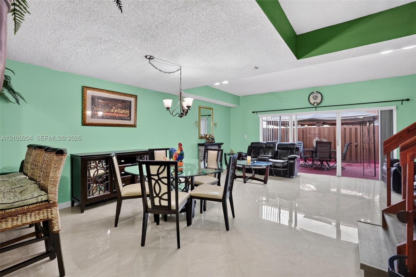 Large-format tile flooring, recessed tray ceiling, sliding glass patio door, and three-arm hanging chandelier