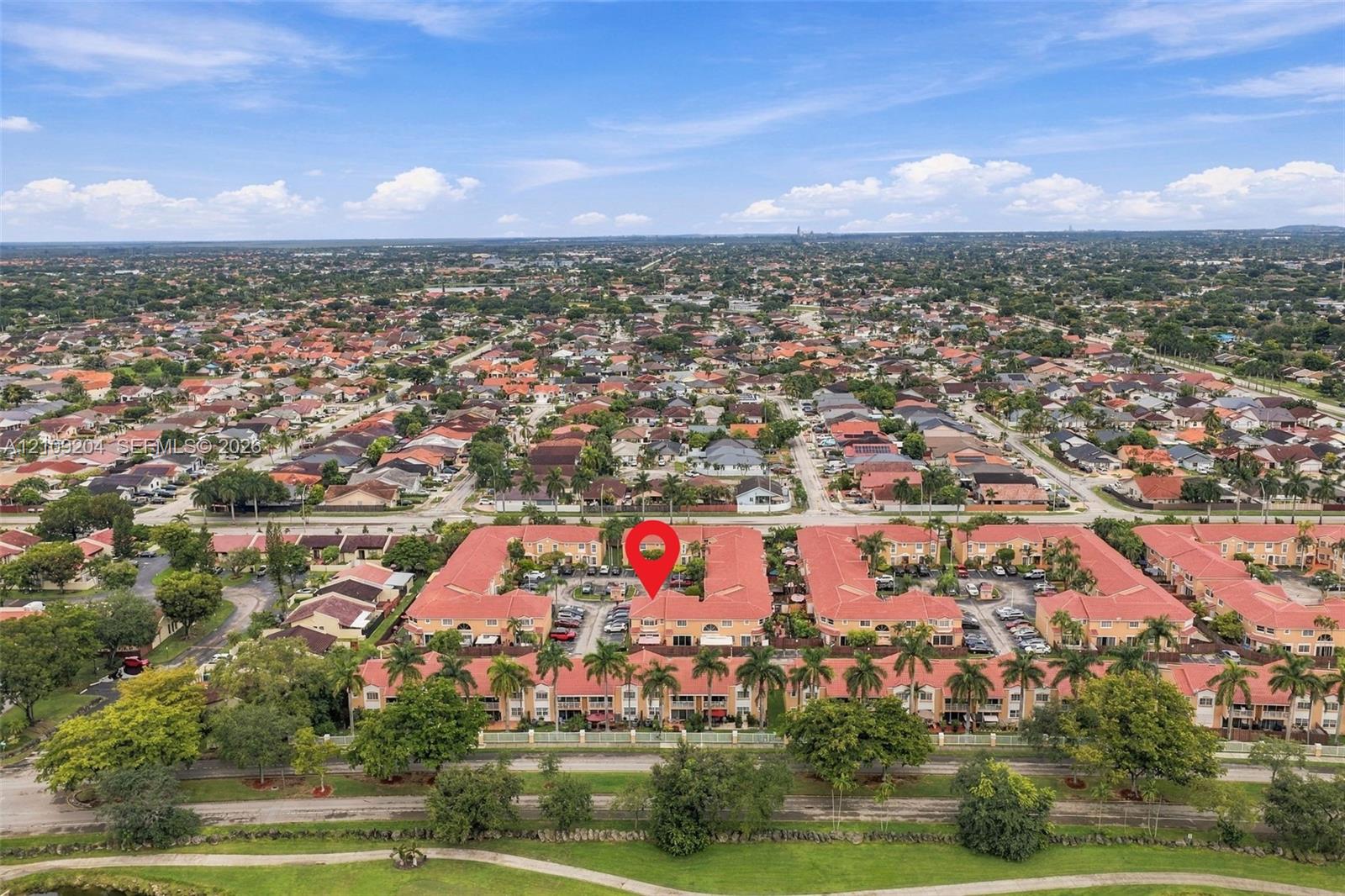 Aerial perspective of a multi-unit residential complex featuring terra cotta-toned roofing, stucco-finish exterior walls, and mature palm tree landscaping