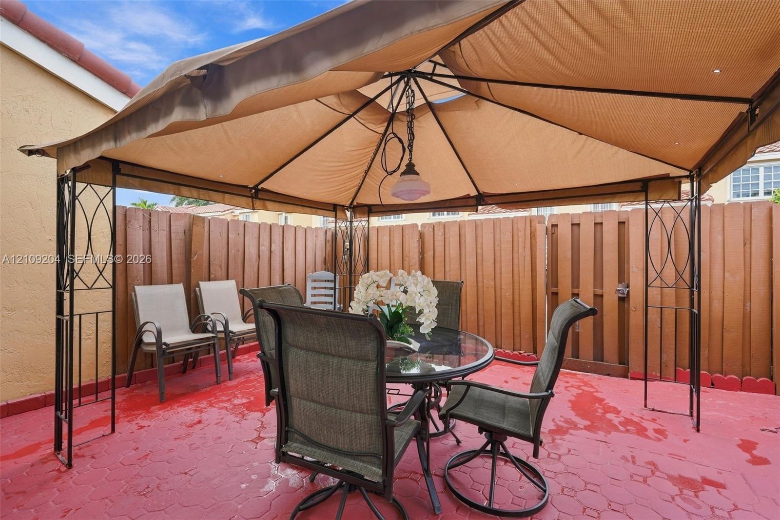 Outdoor patio featuring a paved surface, overhead metal frame canopy, and enclosed wood privacy fencing