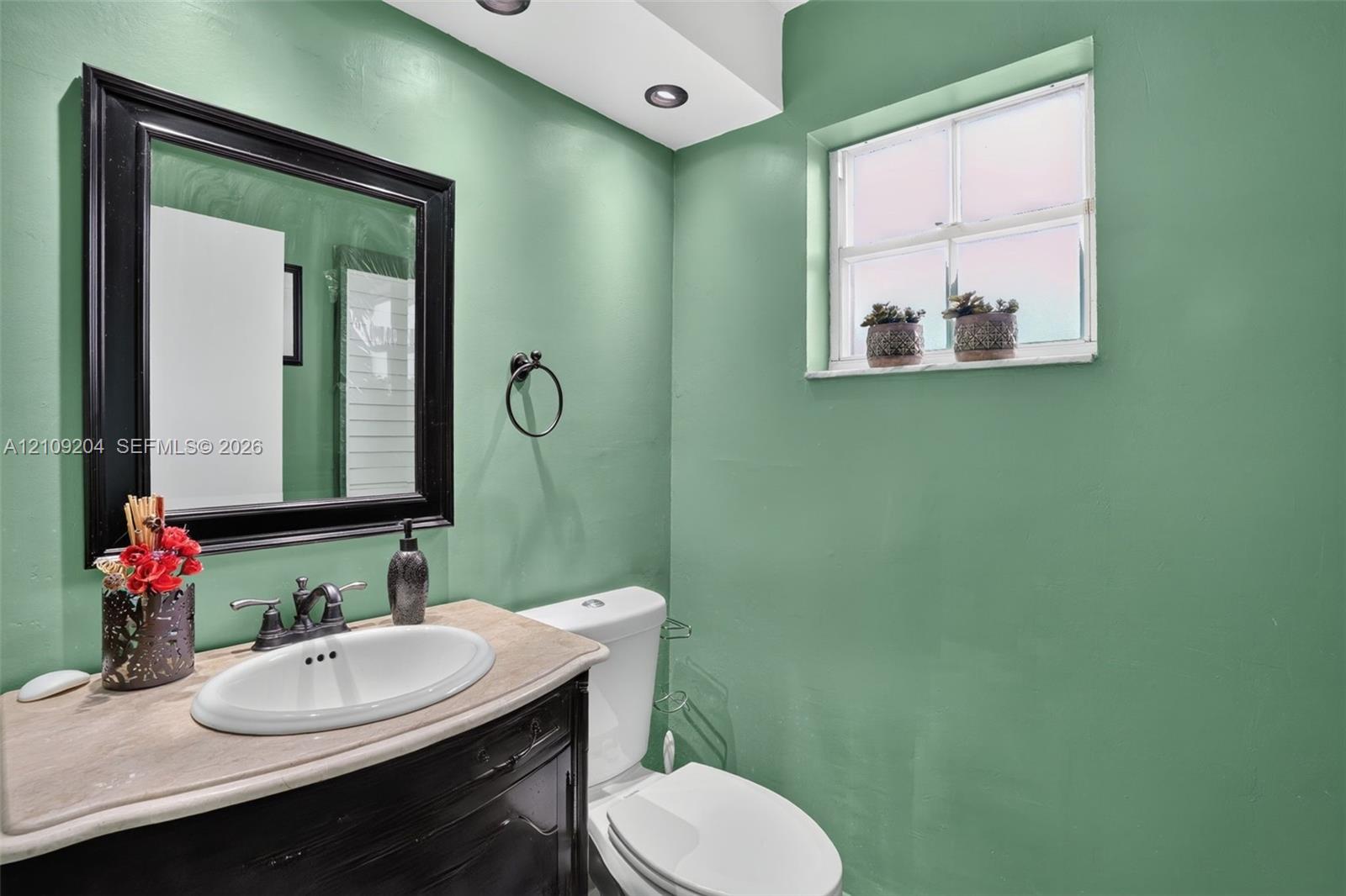 Built-in vanity featuring a stone-surface countertop, integrated oval basin, black-framed mirror, and recessed ceiling lighting Built-in vanity featuring a stone-surface countertop, integrated oval basin, black-framed mirror, and recessed ceiling lighting