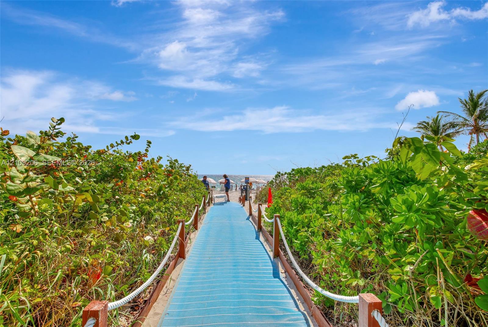 Elevated beach access boardwalk featuring wood posts, rope handrails, and mature coastal vegetation