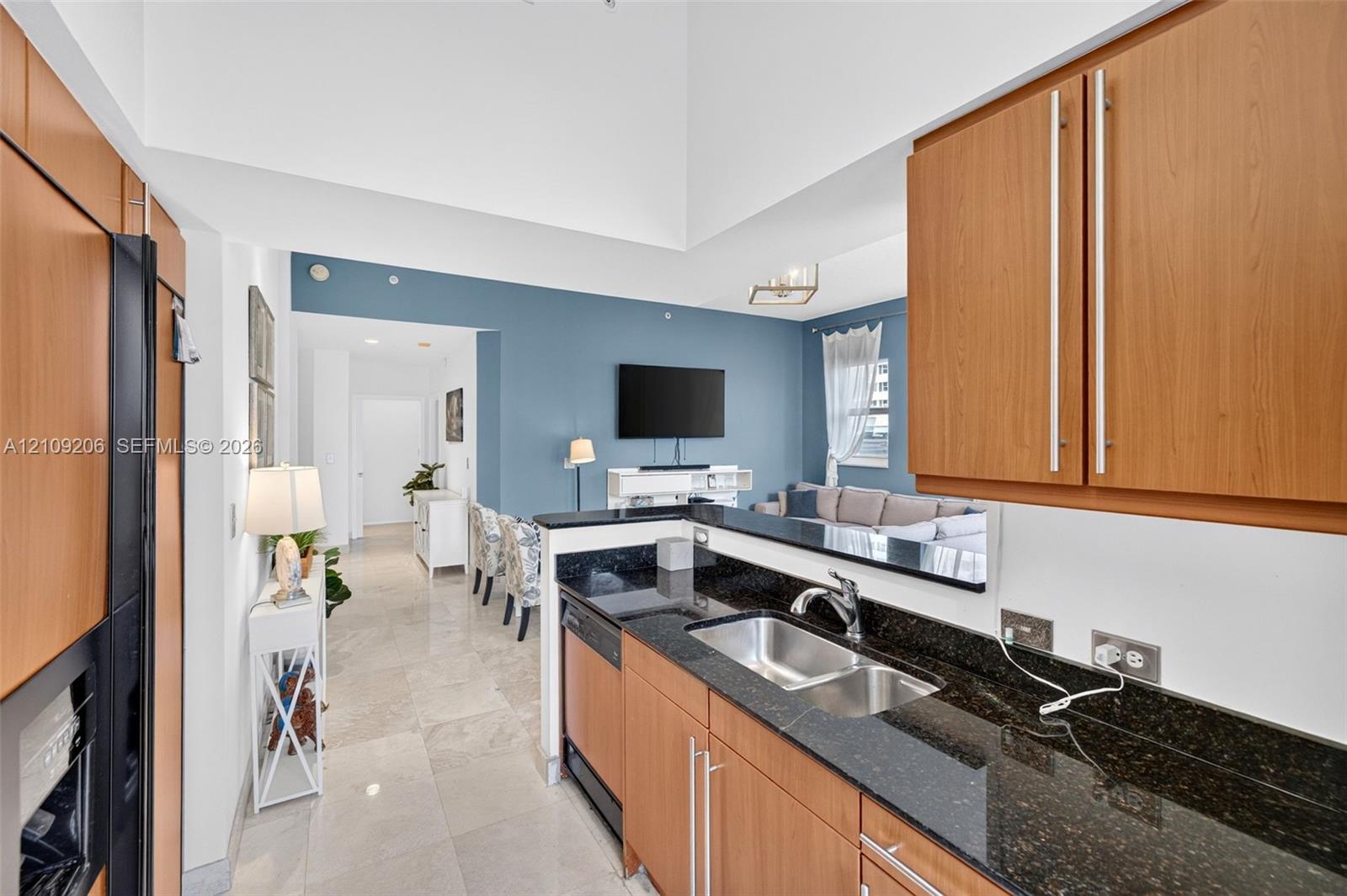 Kitchen featuring wood-finish cabinetry, dark stone countertops, stainless steel dual-basin sink, and tile flooring, set under a vaulted ceiling
