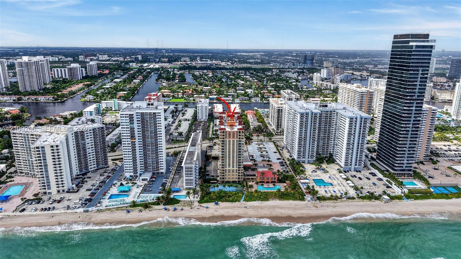 Aerial perspective of coastal high-rise development featuring direct beach access, oceanfront swimming pools, and surface parking areas