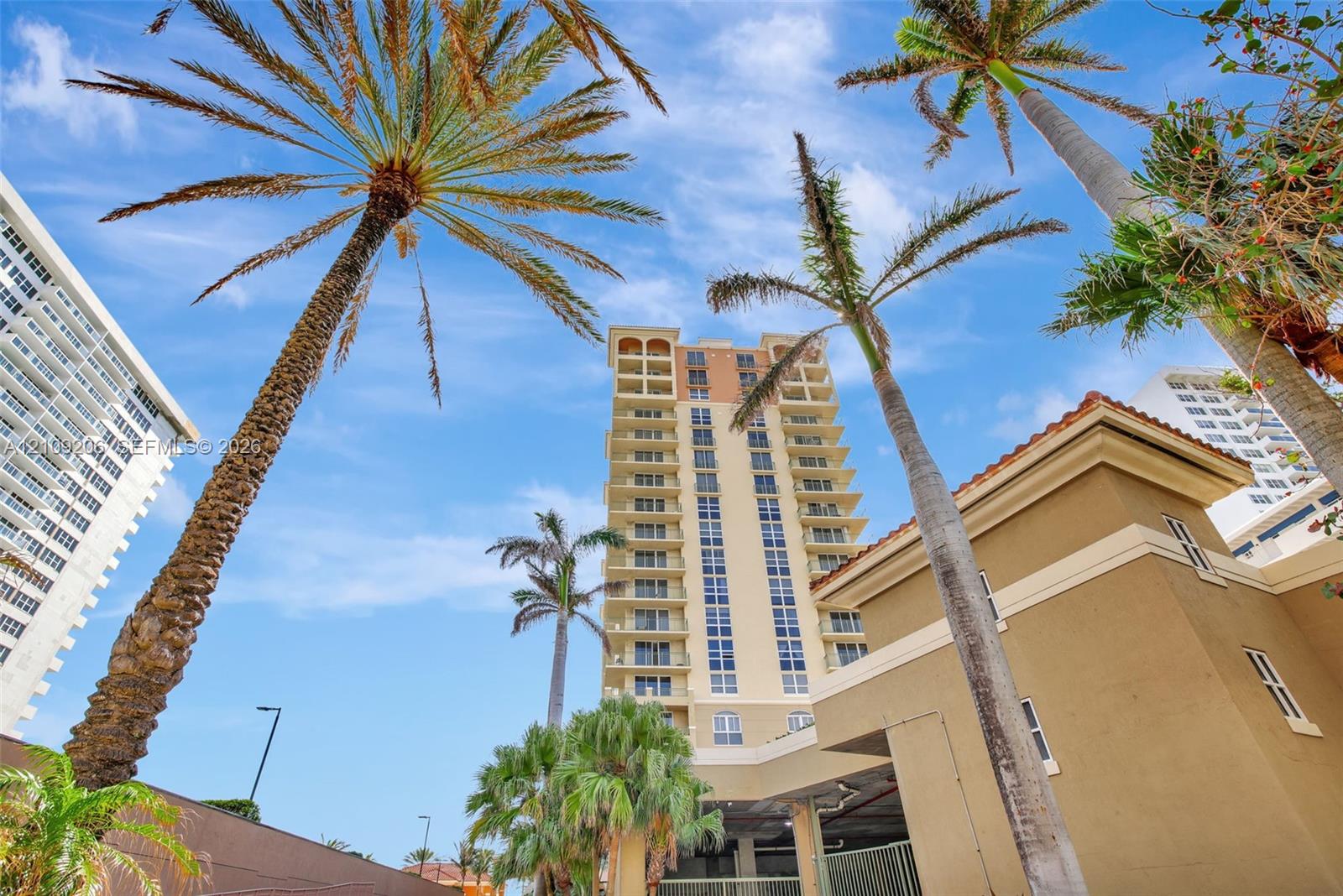 Multi-story residential building exterior featuring a stucco facade, rows of private recessed balconies, and mature palm trees