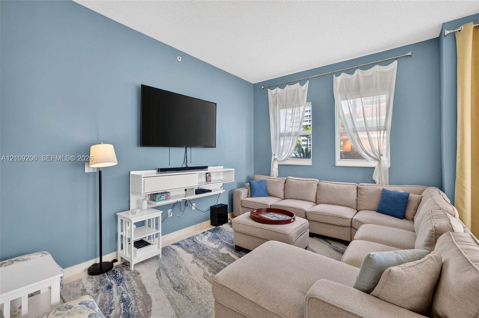 Living area featuring a wall-mounted white media console and two windows with hardware-mounted curtain rods