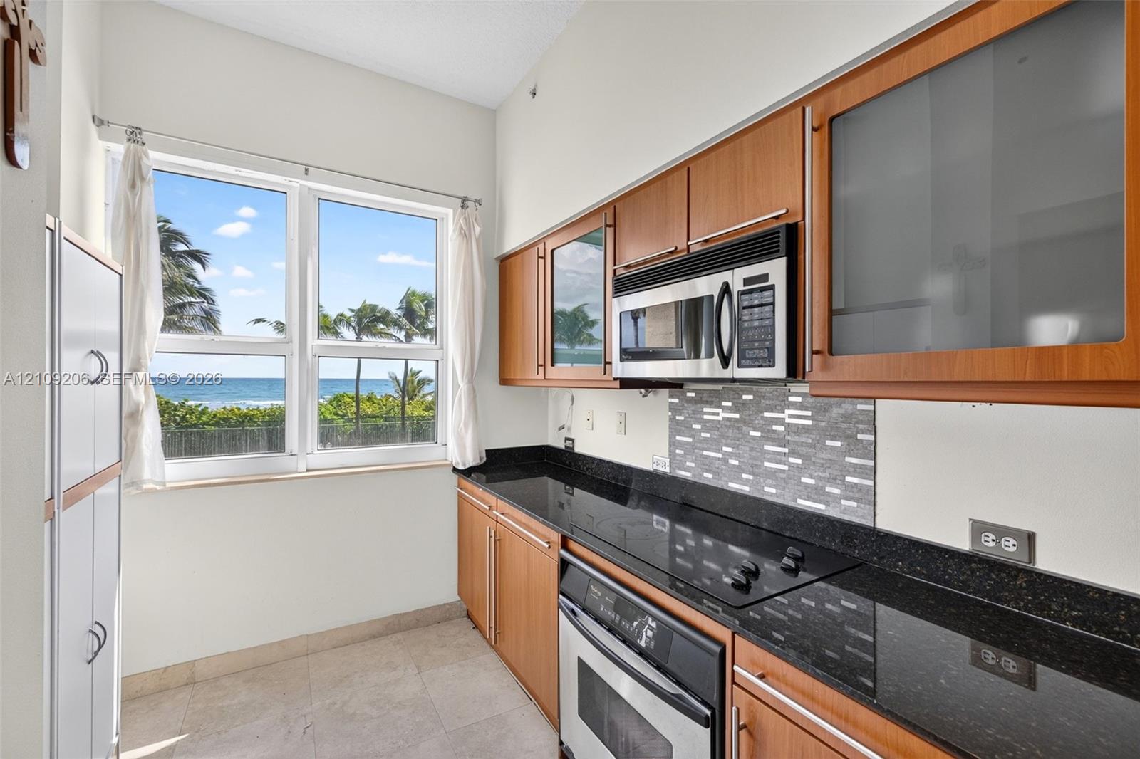 Kitchen featuring wood cabinetry, stone countertops, integrated cooktop, stainless steel microwave, and ocean backdrop