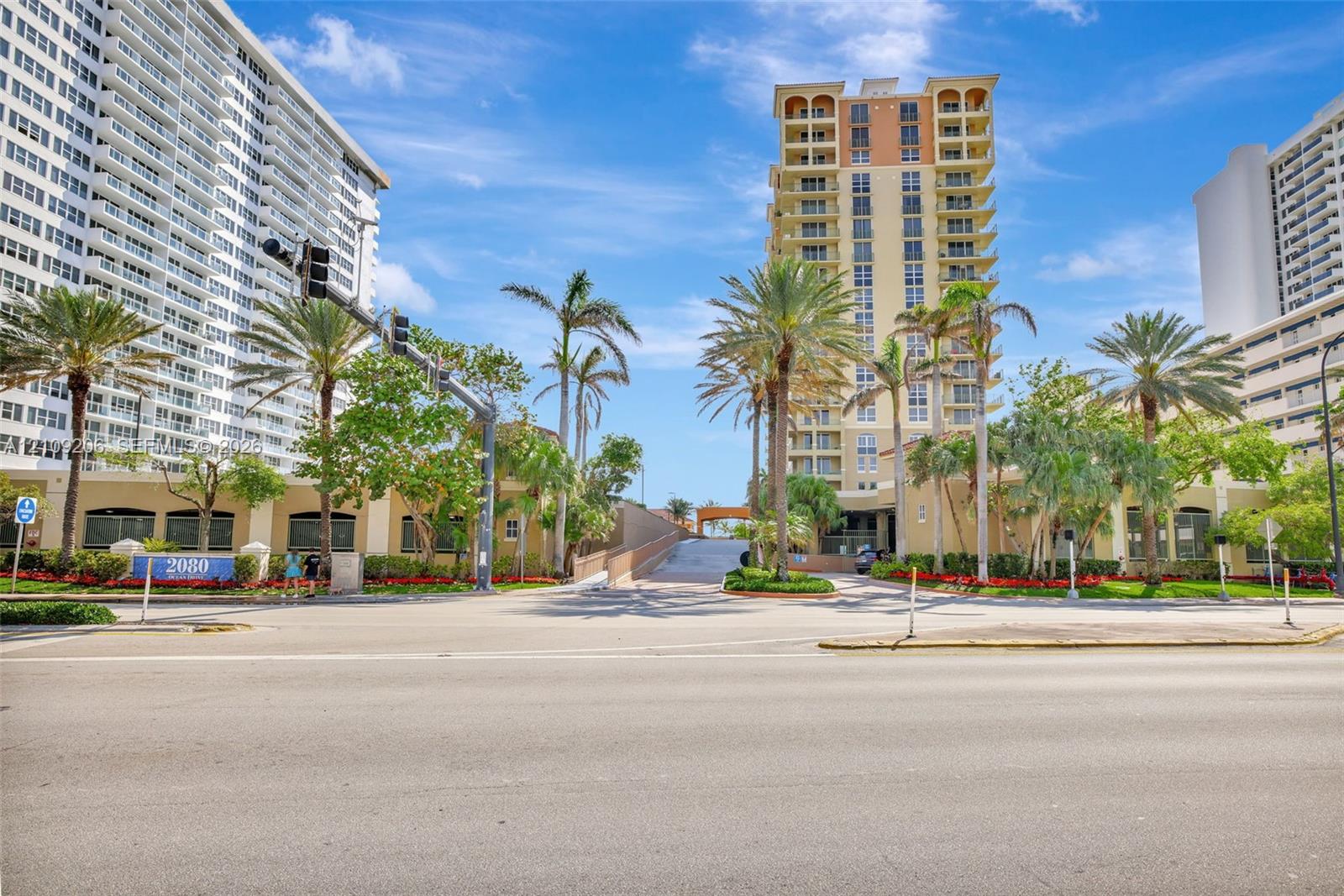 High-rise residential tower featuring arched architectural detailing, private balconies, a multi-story facade, and mature palm tree landscaping