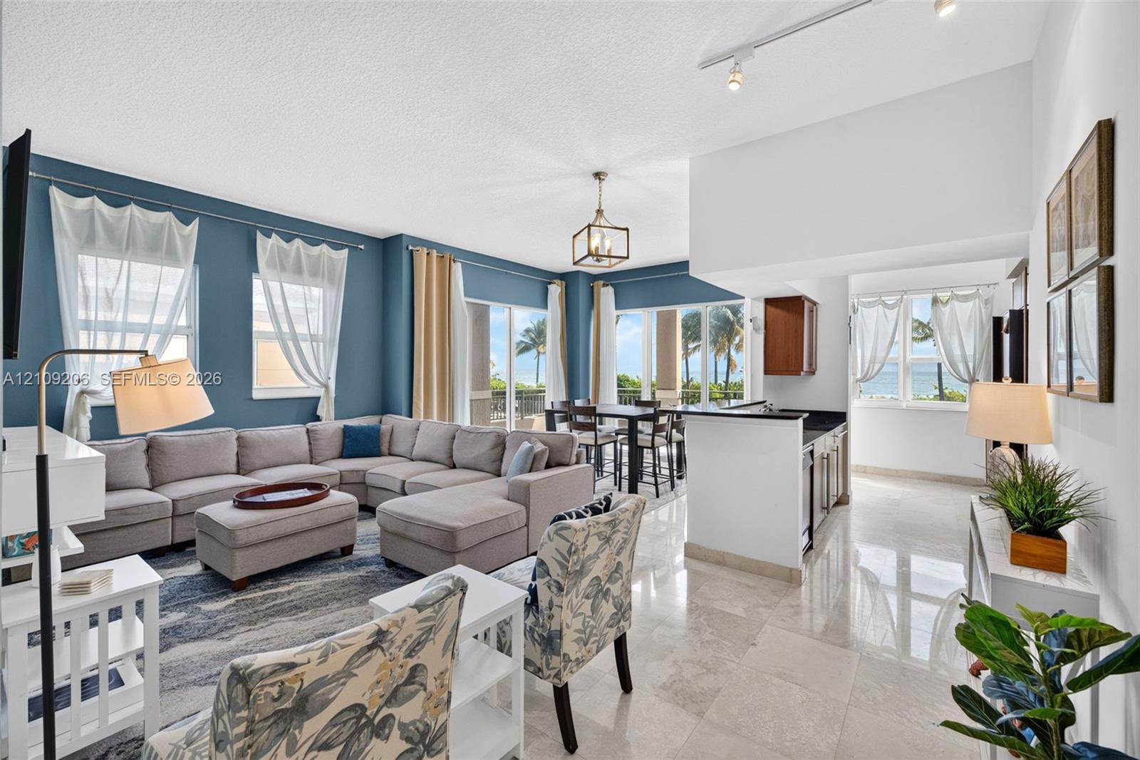 Open-concept interior featuring light-toned stone tile flooring, high ceilings with track and pendant lighting, and floor-to-ceiling glass sliding doors