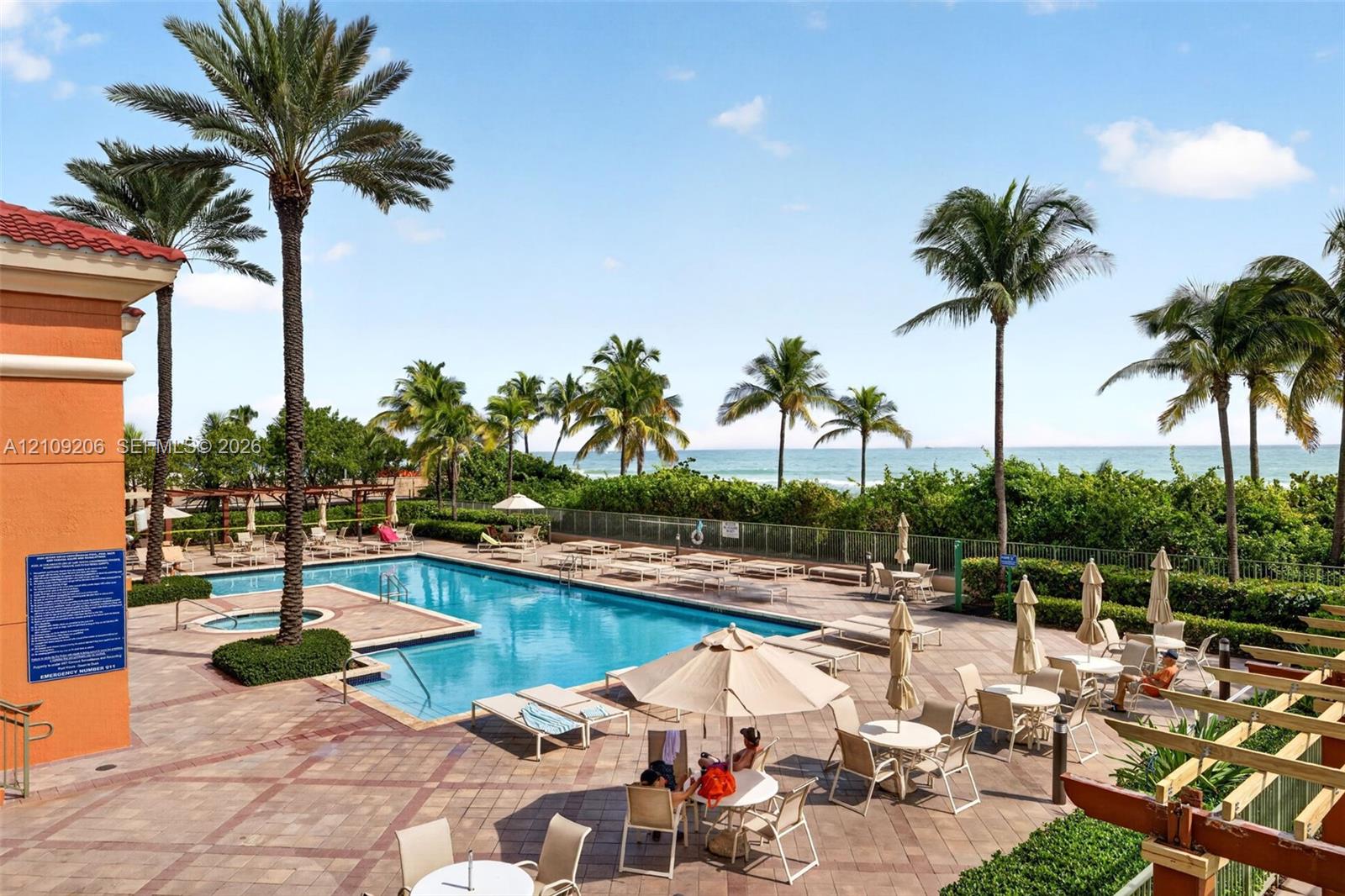 Swimming pool and integrated spa featuring a patterned paver deck, perimeter palm trees, and coastal water backdrop