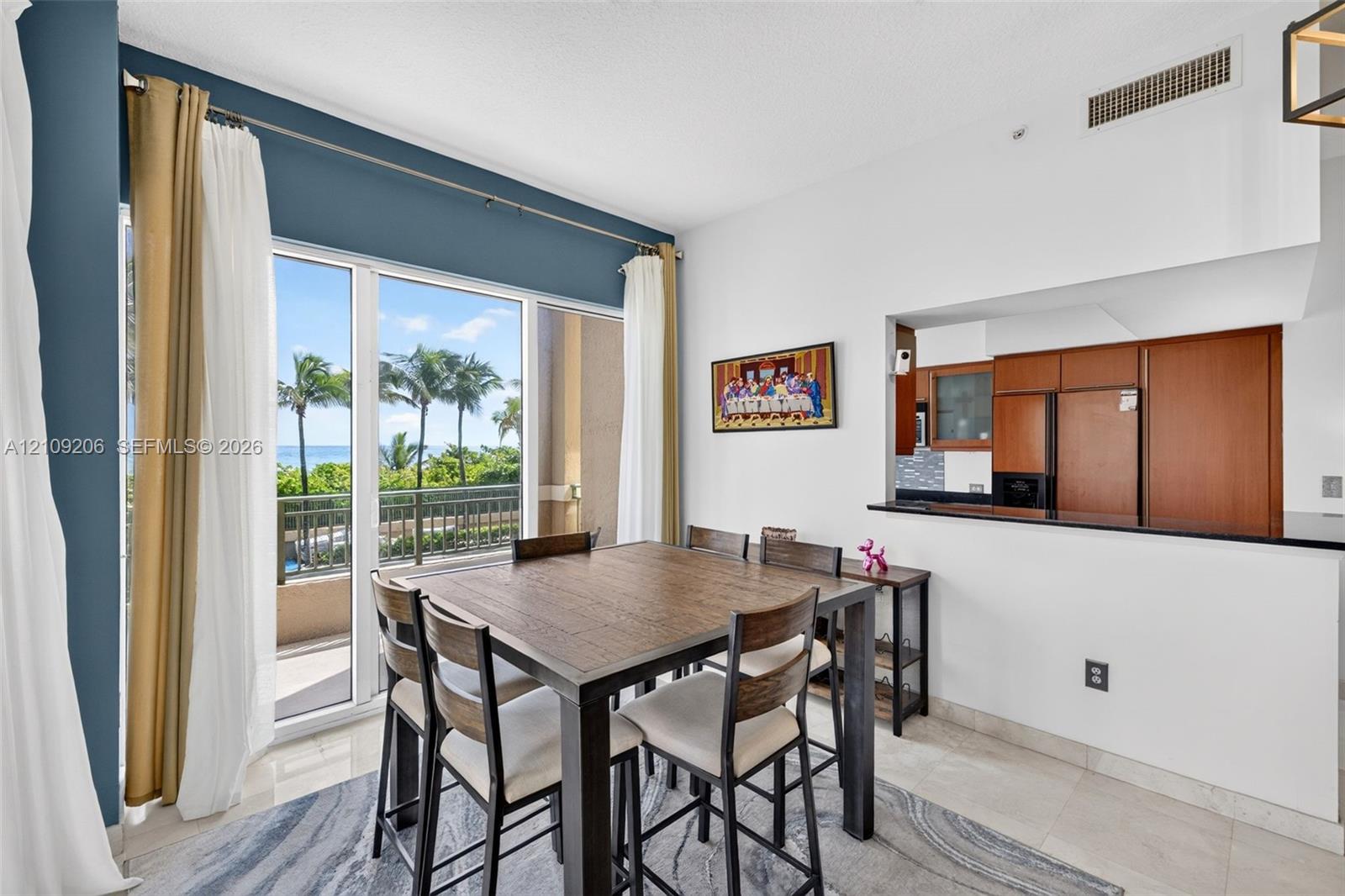 Floor-to-ceiling glass sliding doors with balcony access, kitchen pass-through window with black stone countertop, and tile flooring