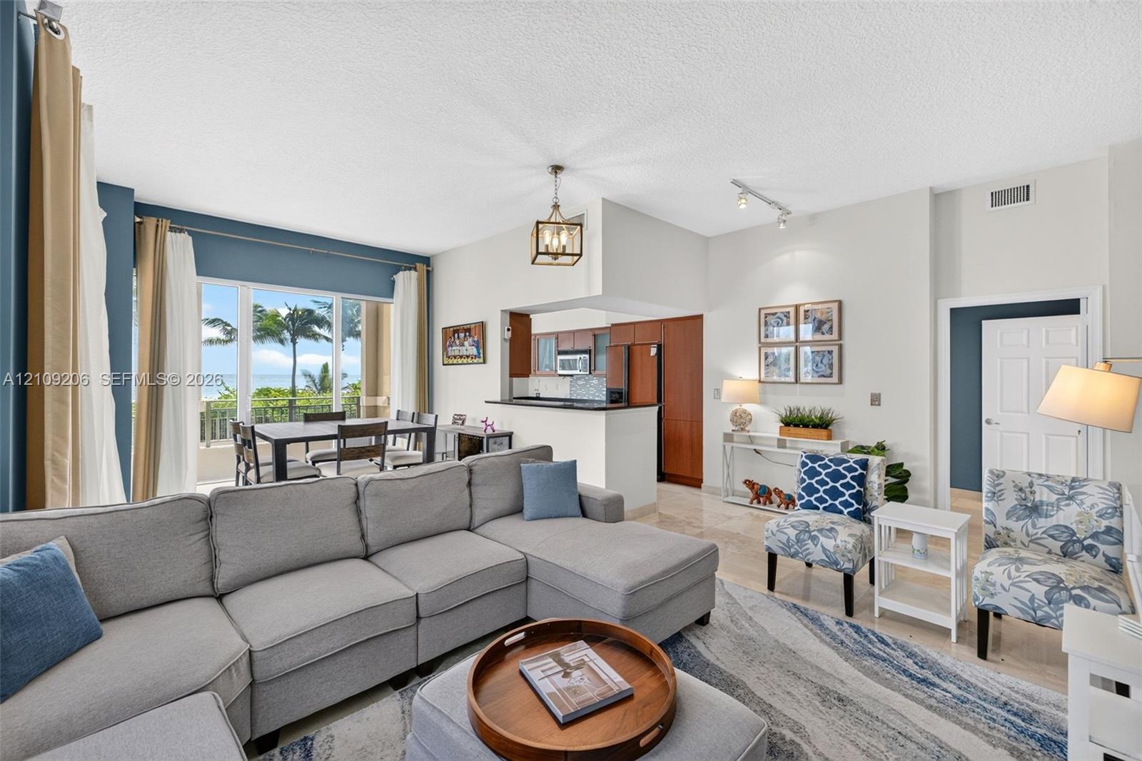 Open-concept interior featuring large windows with coastal scenery, wood cabinetry, polished stone flooring, and a decorative lantern pendant light