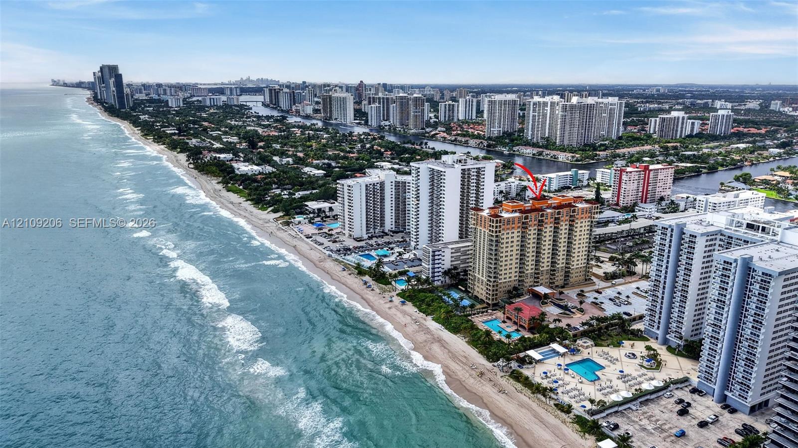 Aerial perspective of high-rise building situated along the coastline featuring proximity to the ocean and paved surface parking