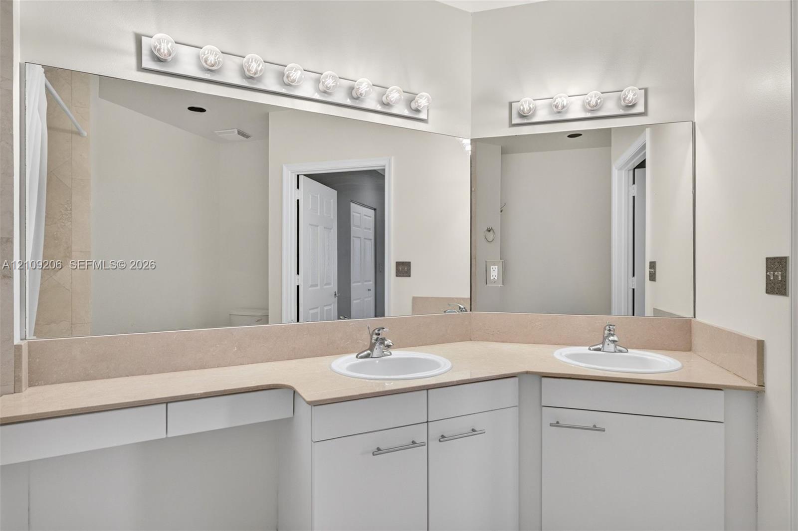 Dual-basin vanity featuring white cabinetry, solid-surface countertop, integrated backsplashes, and wall-mounted light fixtures