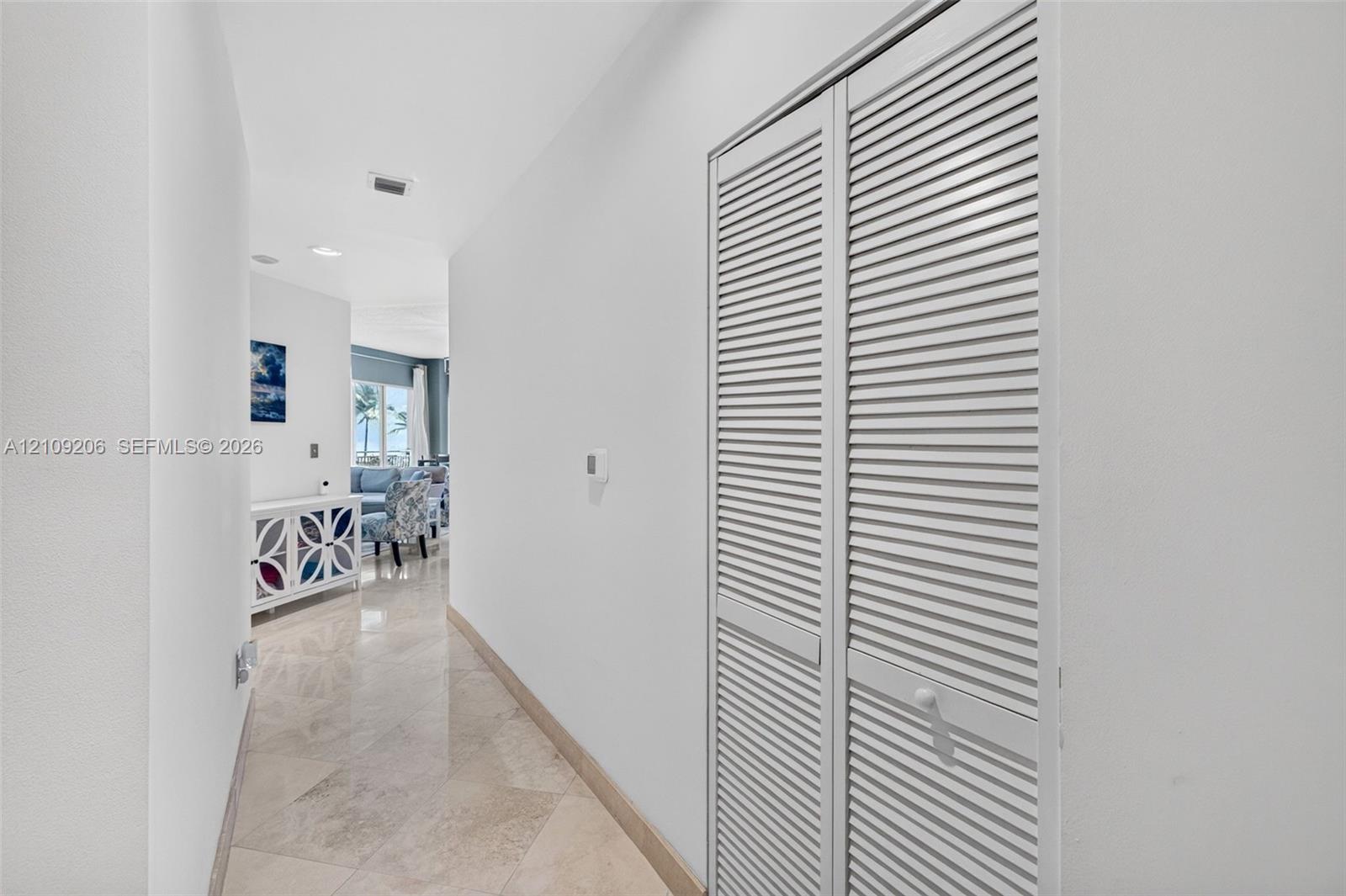 Hallway featuring light-toned stone tile flooring and dual louvered closet doors