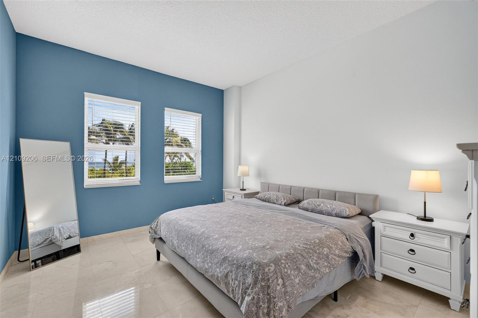 Bedroom featuring two dual-pane windows with integrated blinds, accent-painted wall, and large-format tile flooring