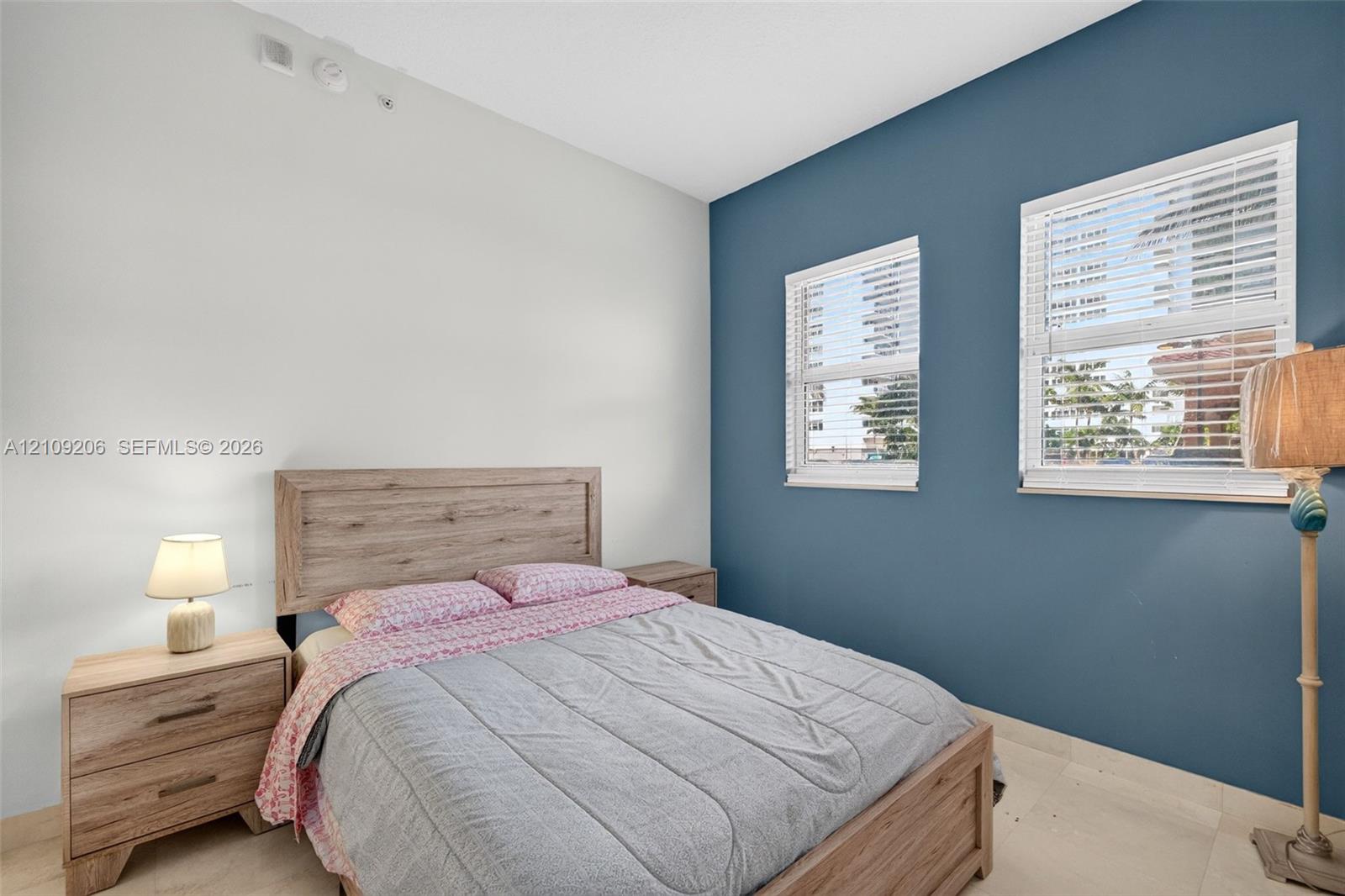 Room featuring a deep blue accent wall, neutral wall tones, two windows with horizontal blinds, and smooth-finish flooring