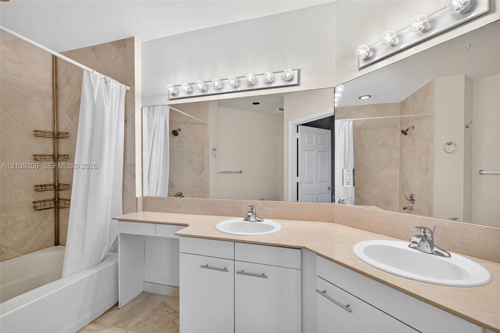 Bathroom featuring a dual-sink vanity with neutral-toned countertops, a large wall-to-wall mirror, built-in cabinetry, and a tub-shower combination with tiled surround