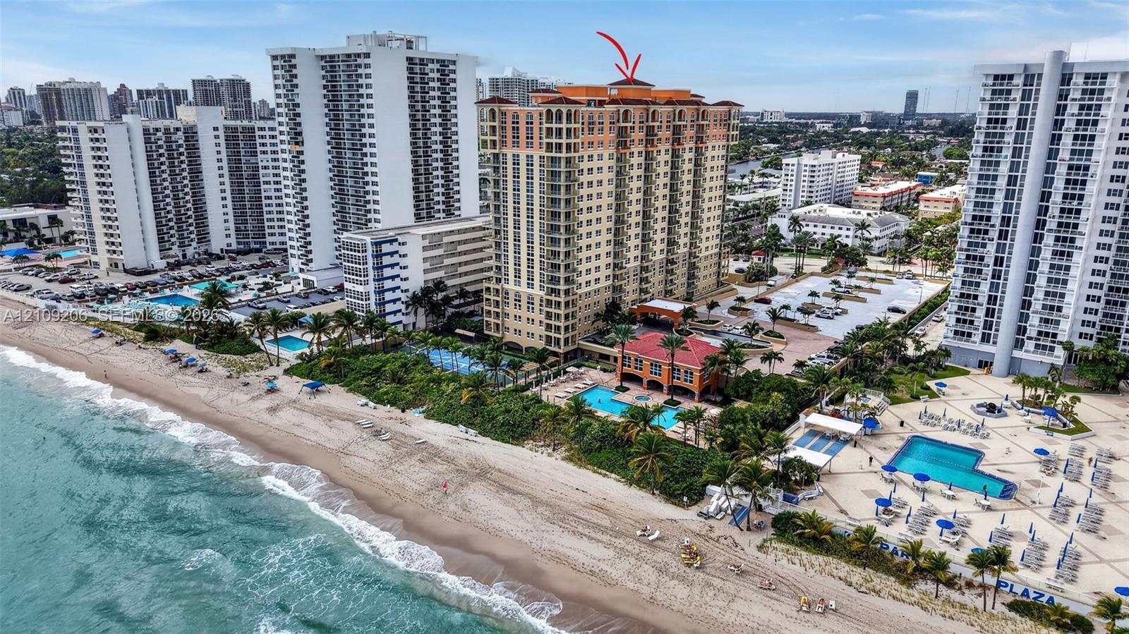 High-rise oceanfront building featuring a tile roof, exterior balconies, a ground-level swimming pool, and direct beach access