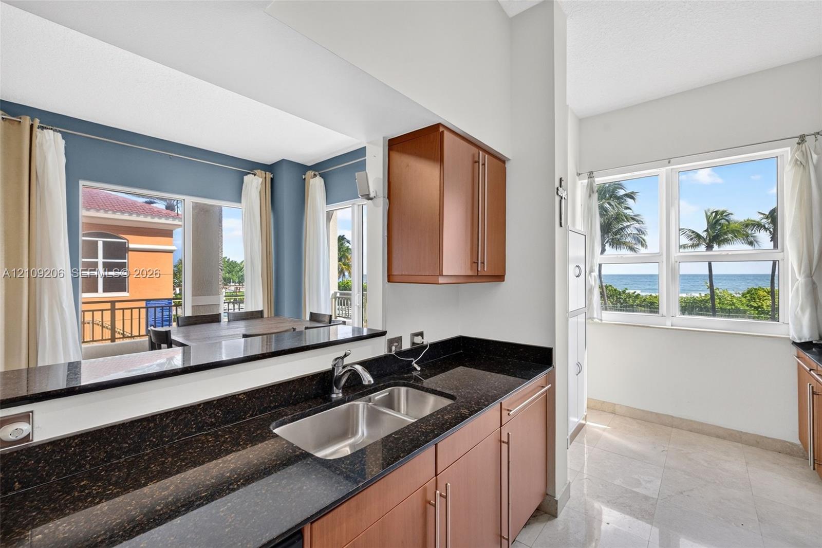 Kitchen featuring dark stone countertops, wood-finish cabinetry, a stainless steel dual-basin undermount sink, and tile flooring