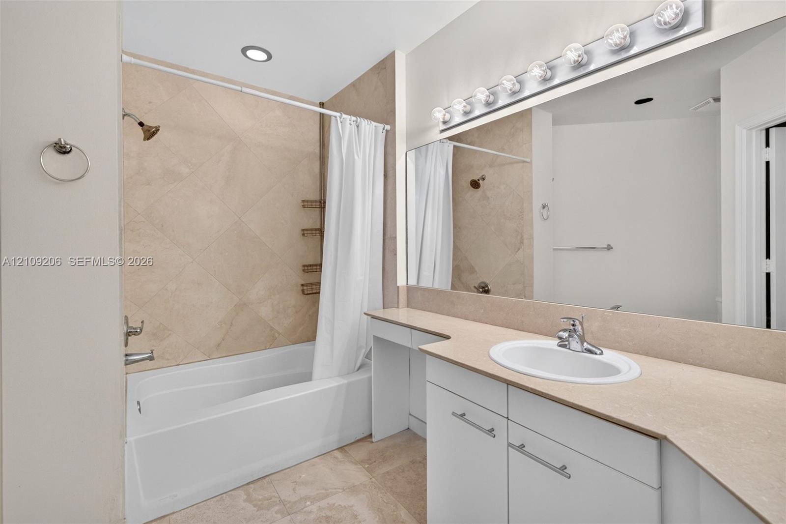 Bathroom featuring a white vanity with a solid surface countertop, an oval under-mount sink, tile-surround tub with a diamond-patterned accent wall, and a large wall-to-wall vanity mirror with integrated multi-bulb lighting
