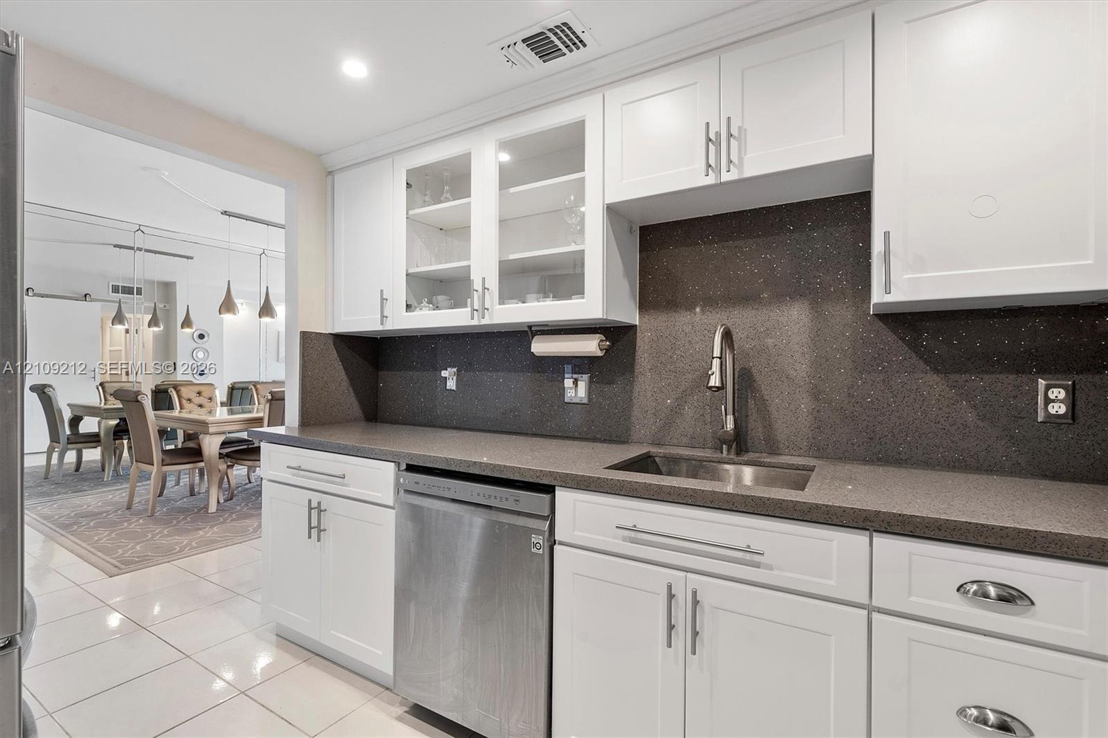 Kitchen featuring white shaker-style cabinetry, glass-front upper cabinet doors, dark-toned solid surface countertops, a stainless steel under-mount sink, and a stainless steel dishwasher