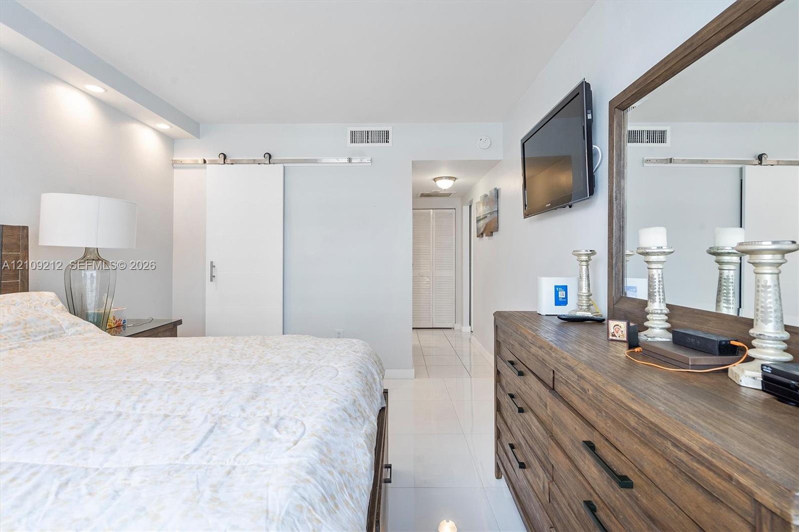 Polished tile flooring, sliding barn door with metallic hardware, recessed ceiling lighting, and double-door closet cabinetry