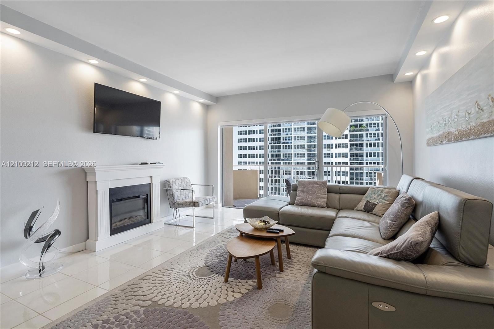 Living area featuring a white fireplace mantel, polished tile flooring, recessed ceiling lighting, and sliding glass doors leading to a balcony Living area featuring a white fireplace mantel, polished tile flooring, recessed ceiling lighting, and sliding glass doors leading to a balcony