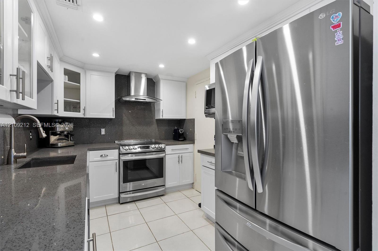 Kitchen featuring white shaker-style cabinetry, quartz countertops, stainless steel appliances, a stainless steel range hood, and tile flooring