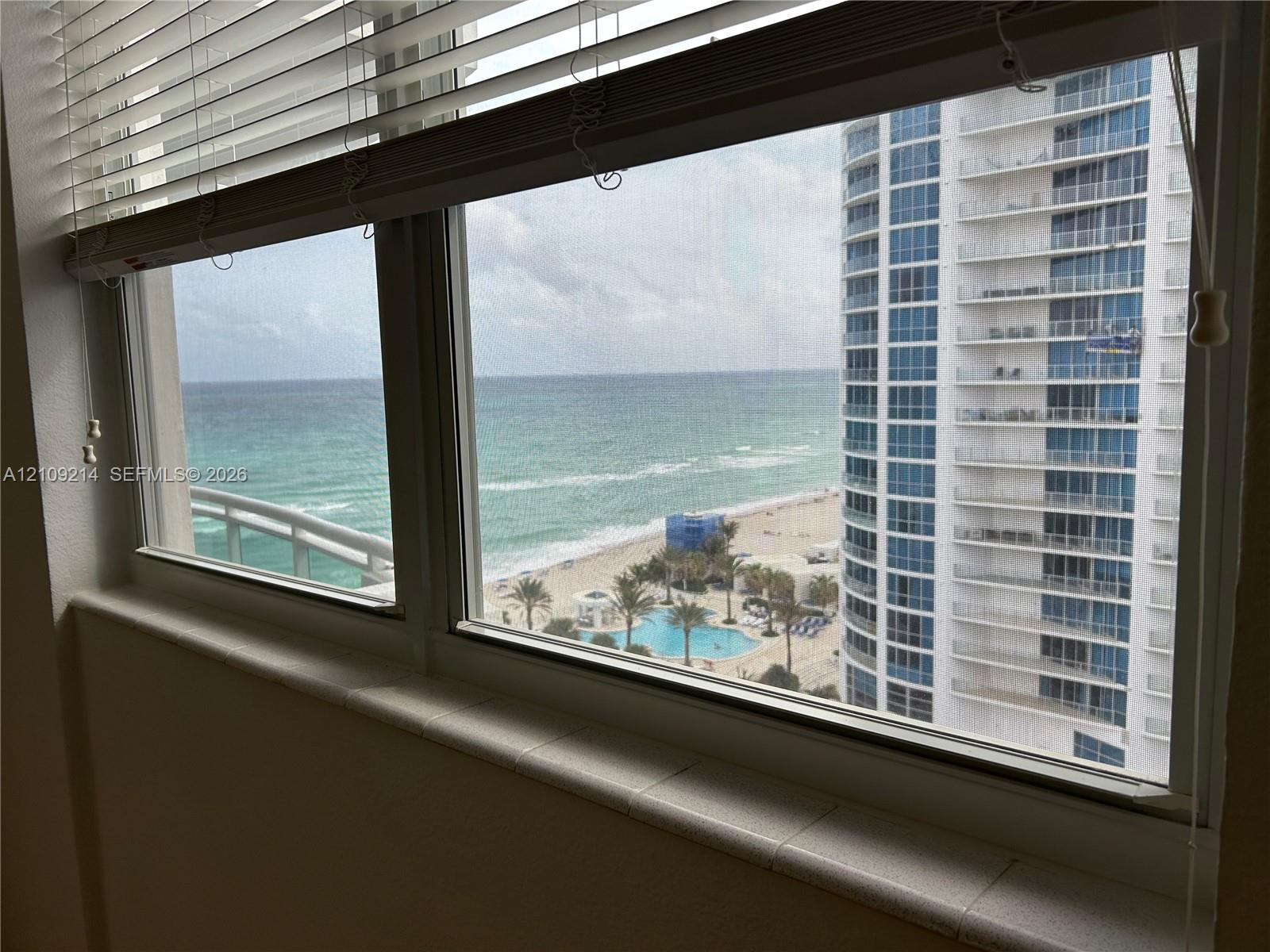 Multi-pane window featuring a wide, tiled sill, horizontal slatted blinds, and expansive ocean and coastal scenery