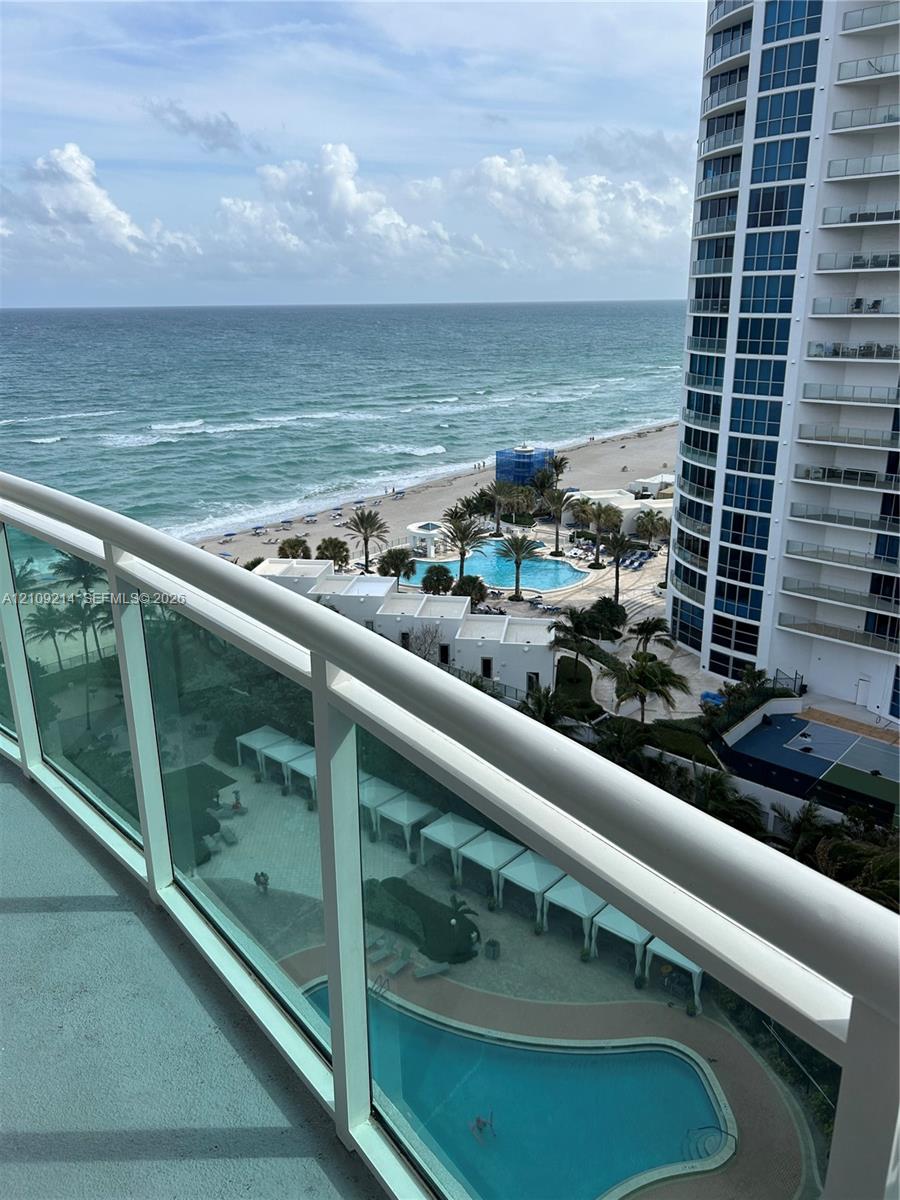 Private balcony featuring glass railings, overlooking a swimming pool, cabanas, and oceanfront shoreline Private balcony featuring glass railings, overlooking a swimming pool, cabanas, and oceanfront shoreline