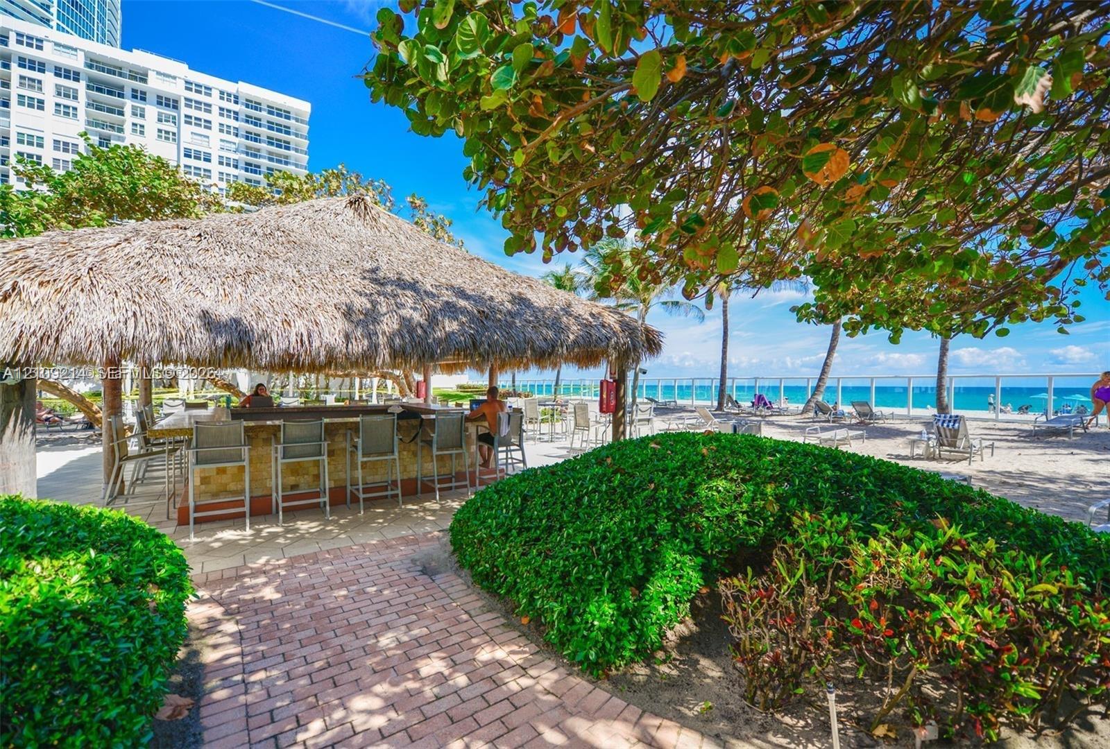 Thatched-roof tiki bar with built-in counter, brick paver pathway, and manicured shrubbery