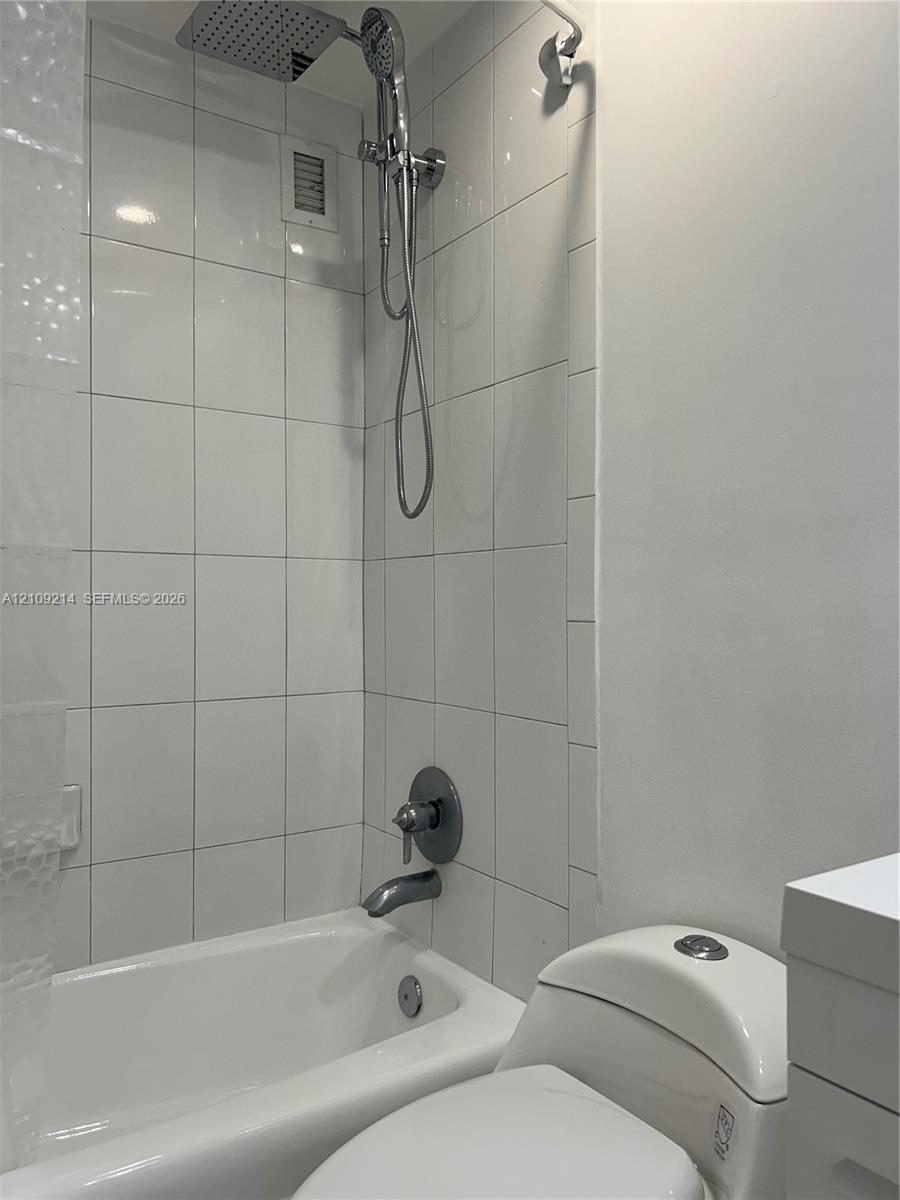Shower and tub combination featuring white wall tiling, a rainfall showerhead, and a handheld shower attachment with metallic fixtures