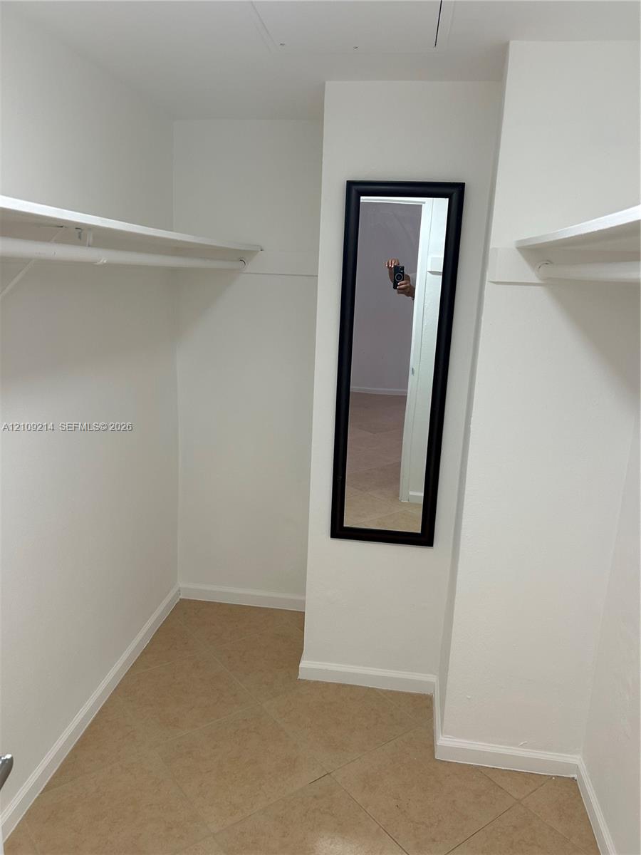 Walk-in storage space featuring ceramic tile flooring, built-in shelving, and a wall-mounted mirror