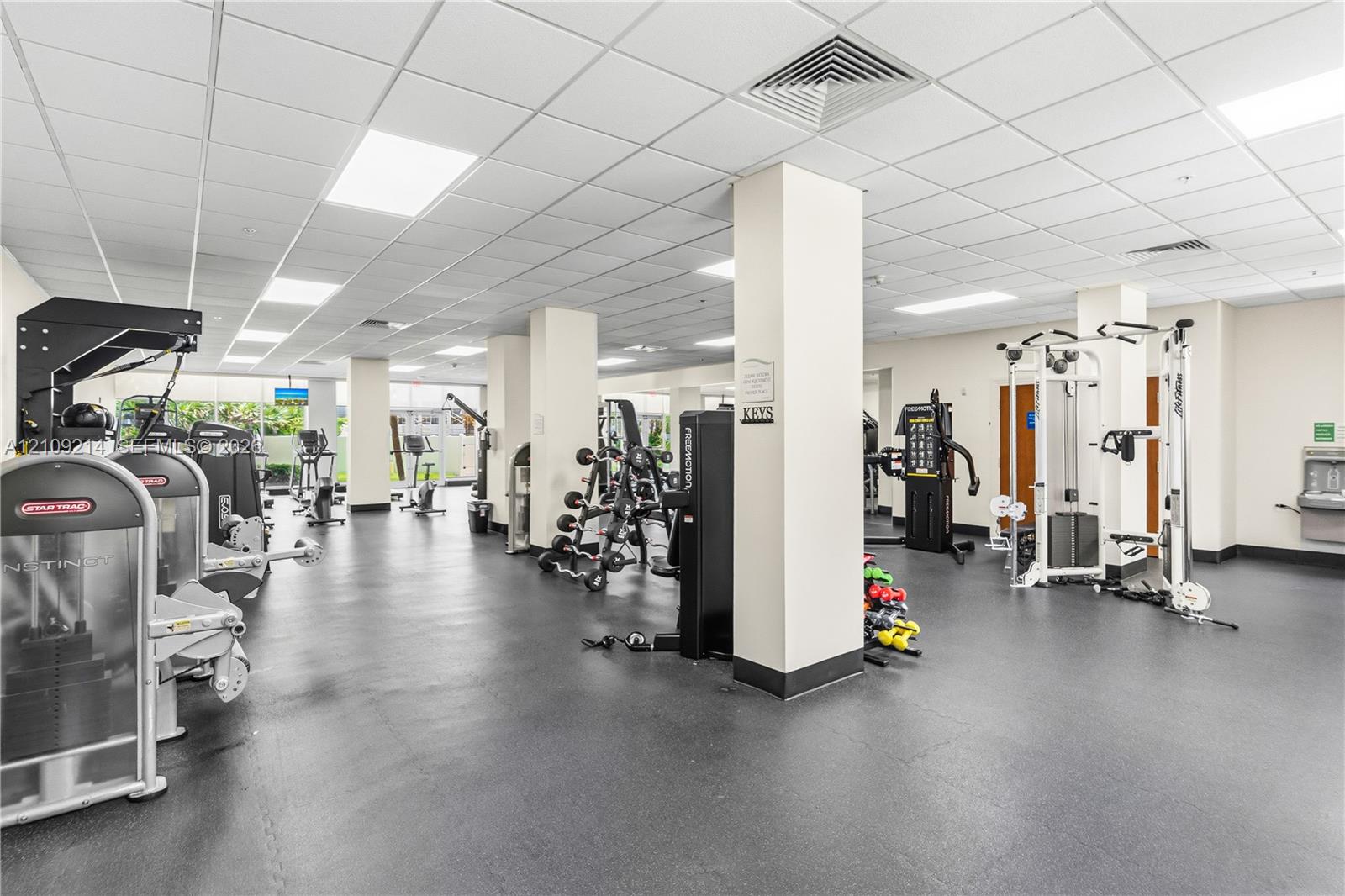 Fitness facility featuring impact-resistant rubber flooring, recessed drop-ceiling grid lighting, and structural support columns