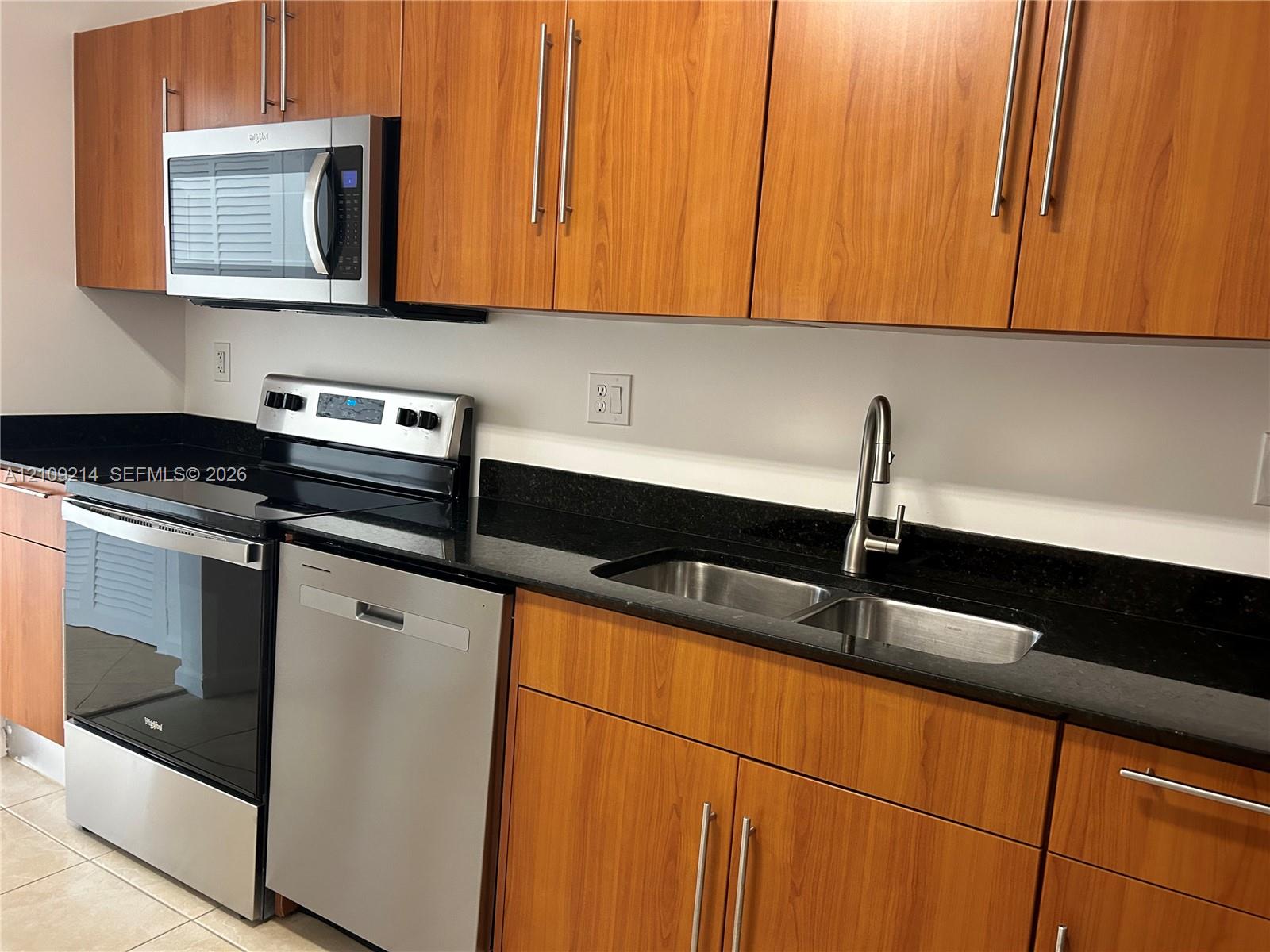 Kitchen featuring flat-panel wood-finish cabinetry, stainless steel appliances, dark countertops, an integrated dual-basin sink with a gooseneck faucet, and tile flooring