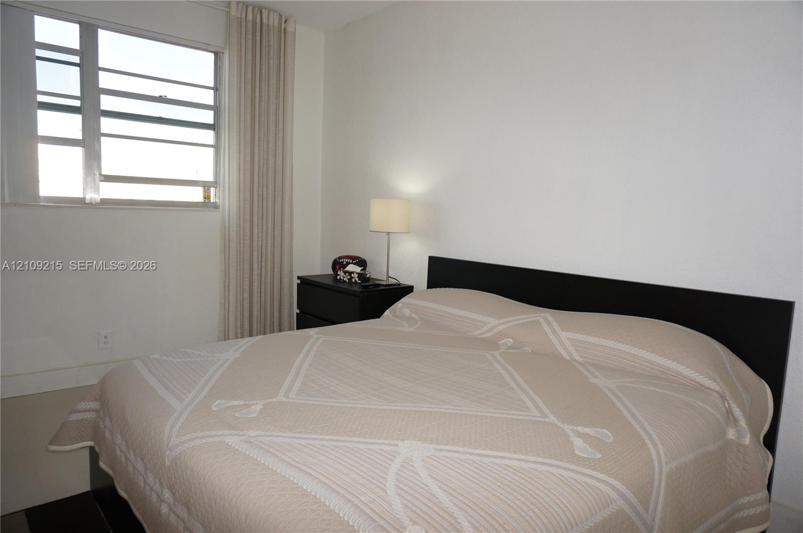 Neutral-toned room featuring a multi-pane louvered window and full-length vertical window treatments