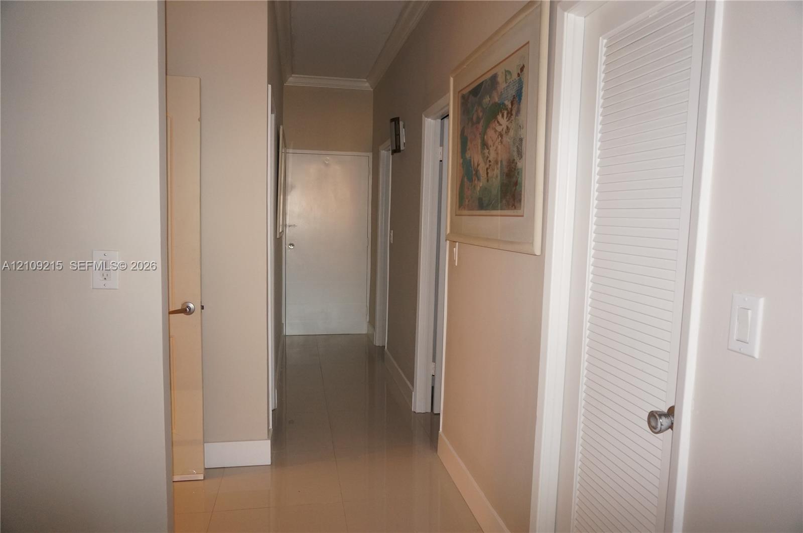 Hallway featuring neutral-toned walls, crown molding, polished tile flooring, and a louvered bi-fold closet door