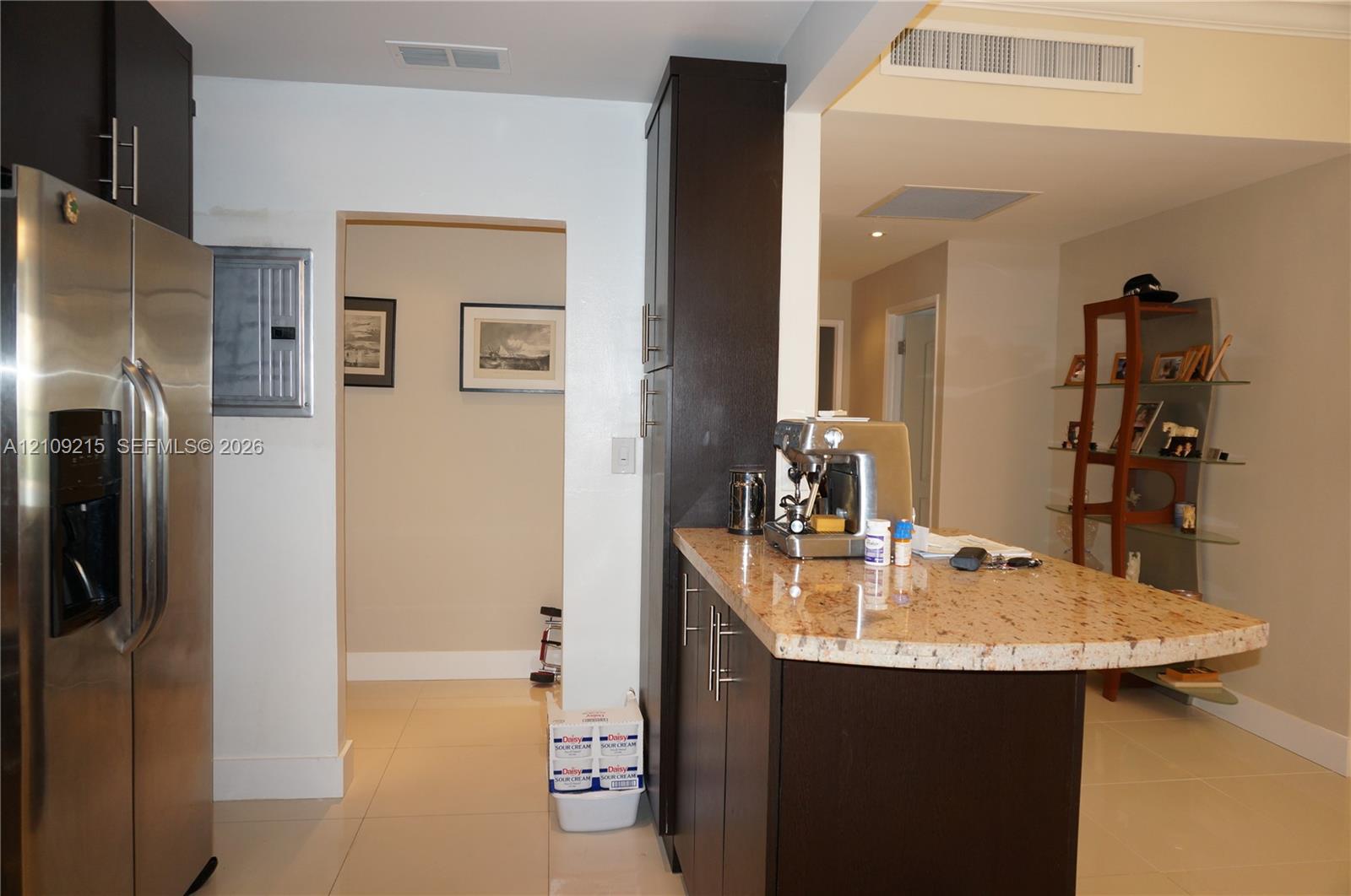 Kitchen featuring dark wood-finish cabinetry, a stone-surface peninsula, stainless steel refrigerator, and tile flooring