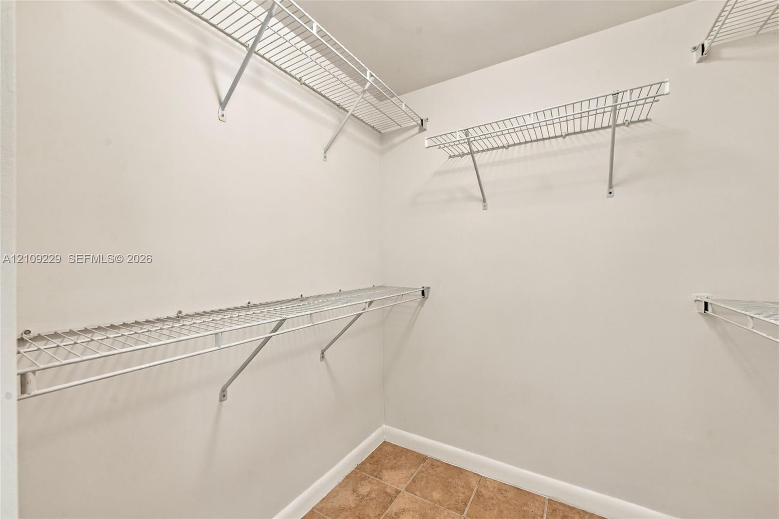 Storage area featuring white walls, tiled flooring, and multiple tiers of installed white wire shelving