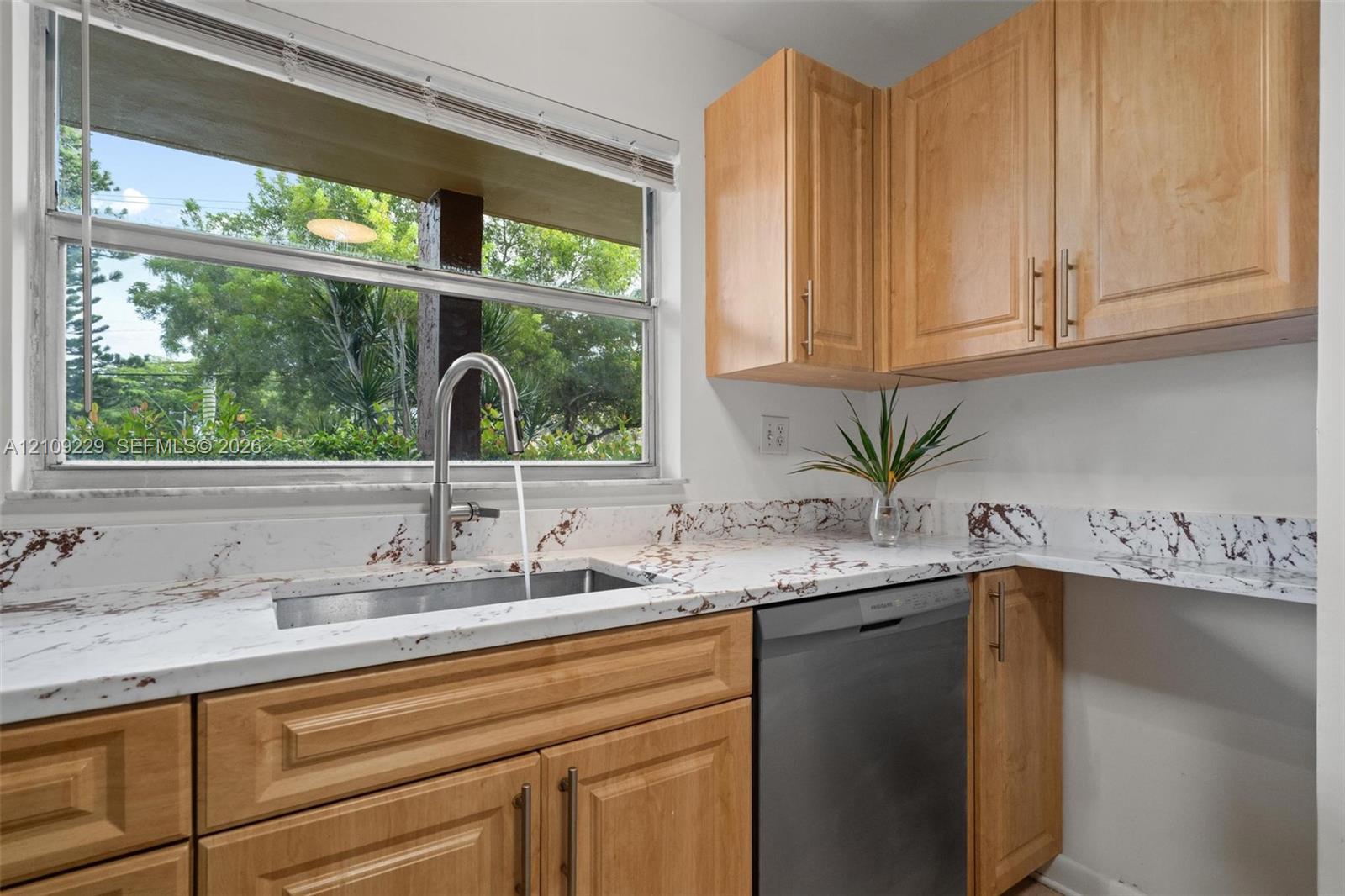 Kitchen featuring shaker-style wood cabinetry, stone-patterned countertops, undermount stainless steel sink, gooseneck faucet, and stainless steel dishwasher